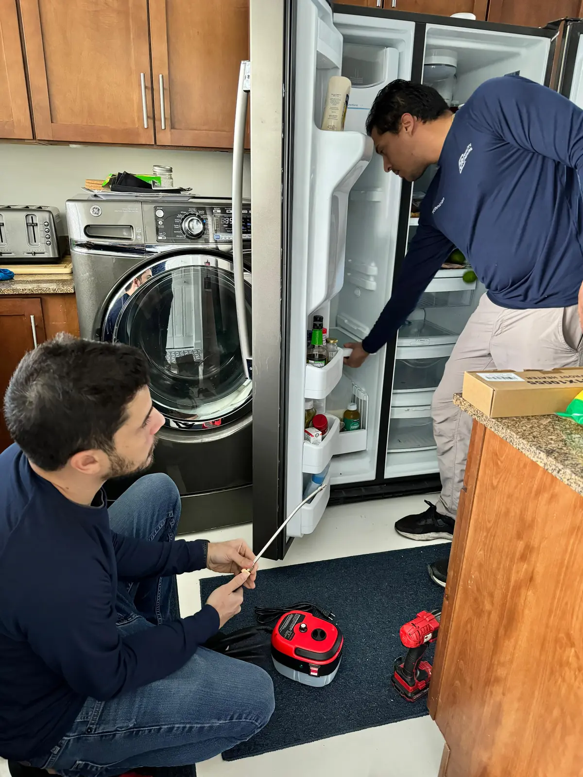 Two Quality Repairs technicians diagnosing a side-by-side refrigerator