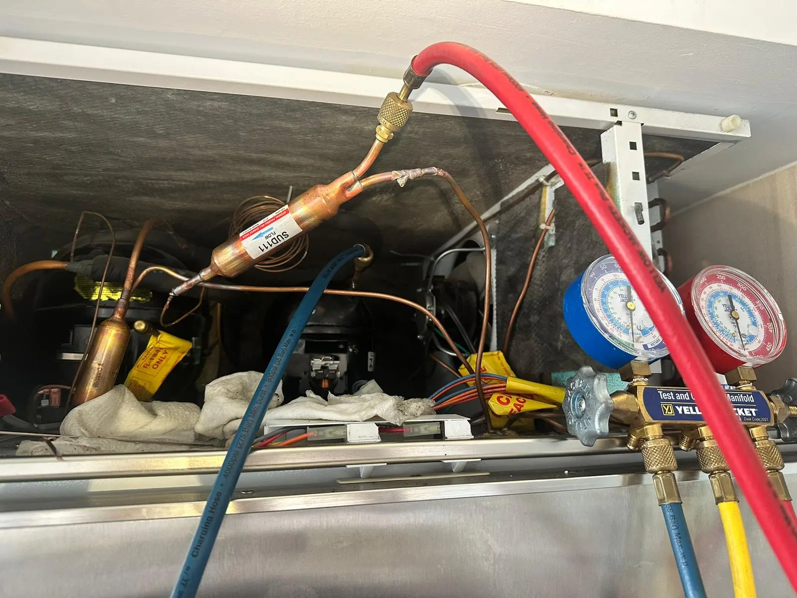 Refrigerant manifold gauges and hoses connected to a refrigerator compressor area